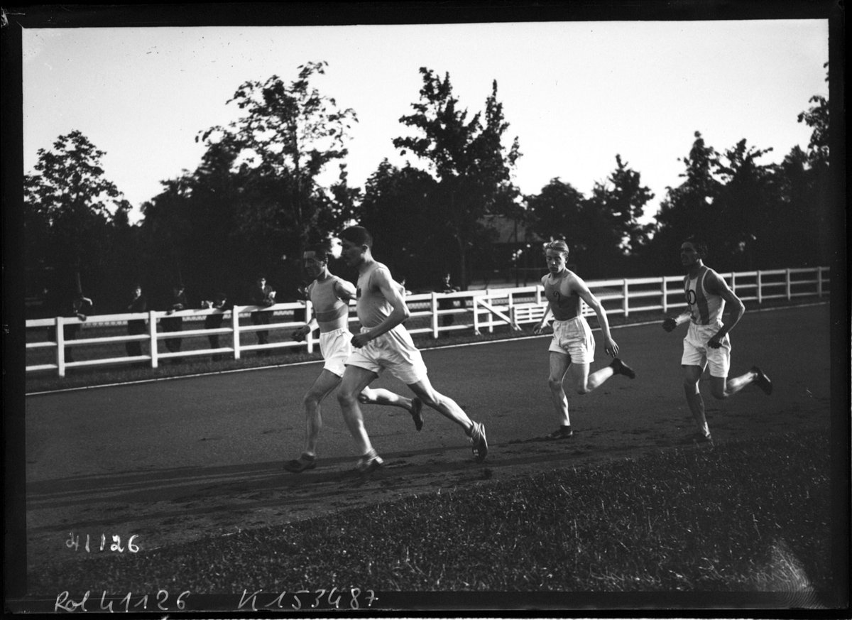Photographie ancienne de trois coureurs sur une piste en cendrée bordée d'une barrière blanche
