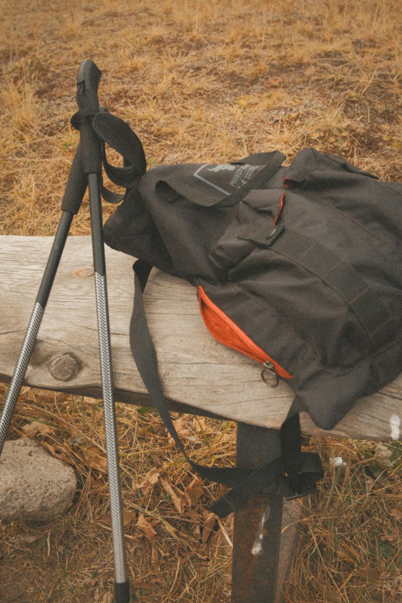 Bâtons de marche et petit sac à dos posés contre une barrière en bois au bord d'un chemin