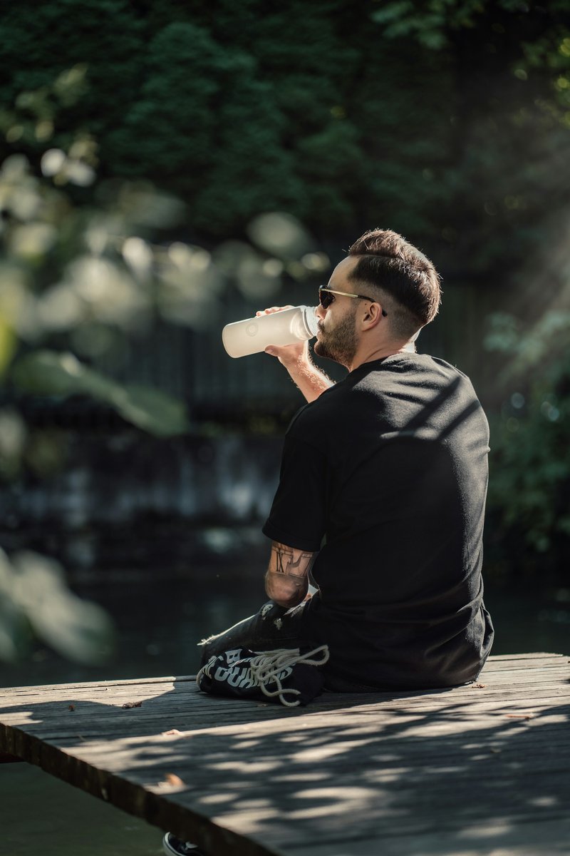 Sportif assis de dos sur un banc en bois, qui boit à la gourde à l'ombre des arbres