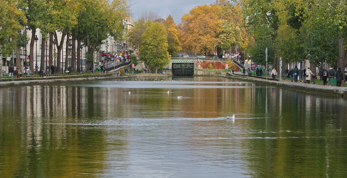 Un canal parisien bordé d'arbres à l'automne, avec une passerelle au fond