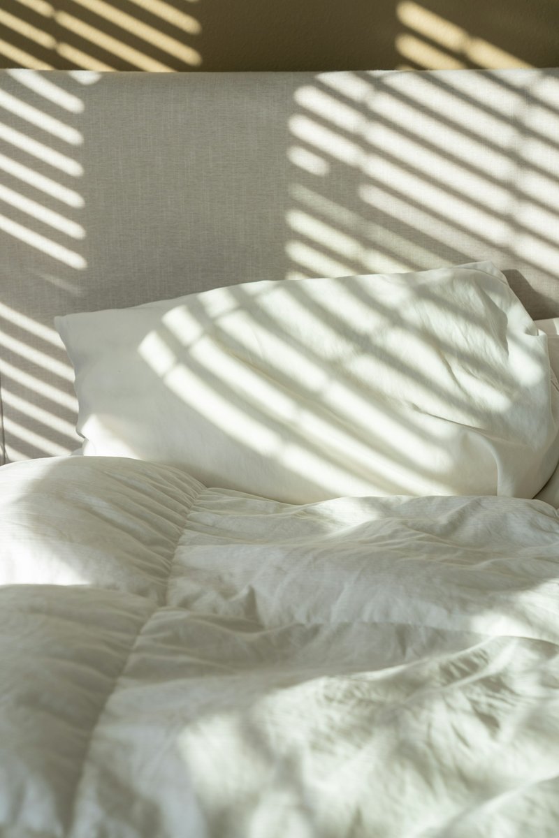 Lit aux draps froissés éclairé par le soleil qui passe à travers des stores