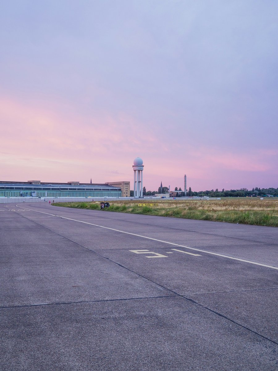 Ancienne piste d'aéroport en béton au crépuscule, avec la tour radar et le terminal au loin