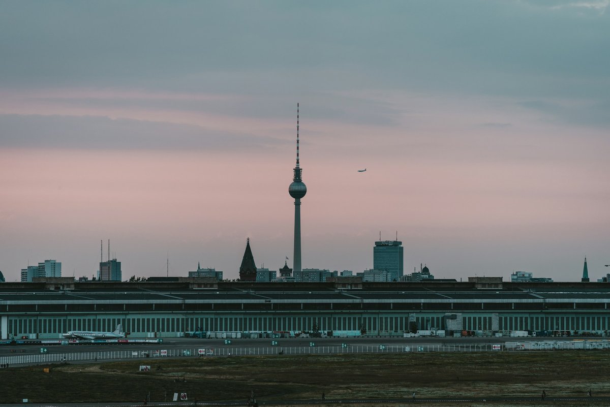Grande étendue d'herbe au premier plan et silhouette de la tour de télévision de Berlin à l'horizon