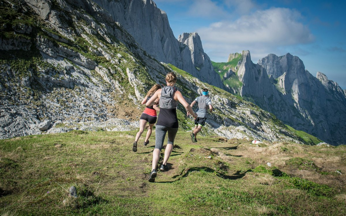 Deux coureurs de trail de dos dans un alpage, au pied d'aiguilles rocheuses