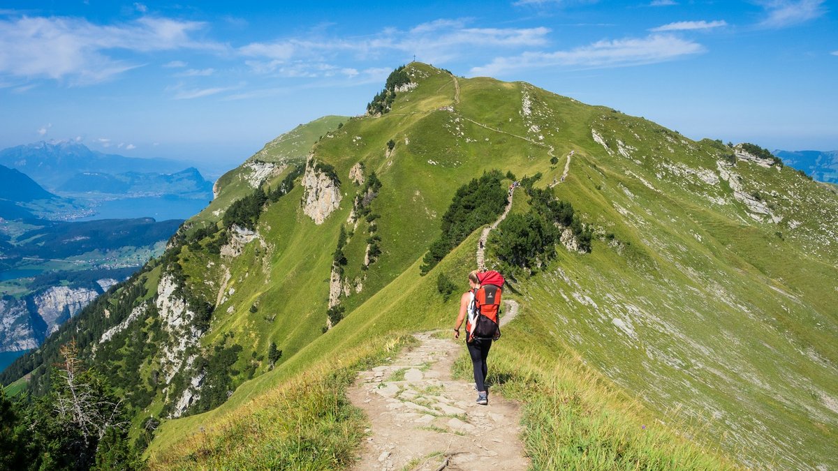 Coureur vêtu de rouge sur un sentier de crête herbeux qui domine un lac de montagne